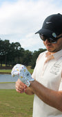 Man on a golf course wearing sunglasses and a Mulligan Hooligan ball marker, admiring the ''I'm a simple man'' golf glove