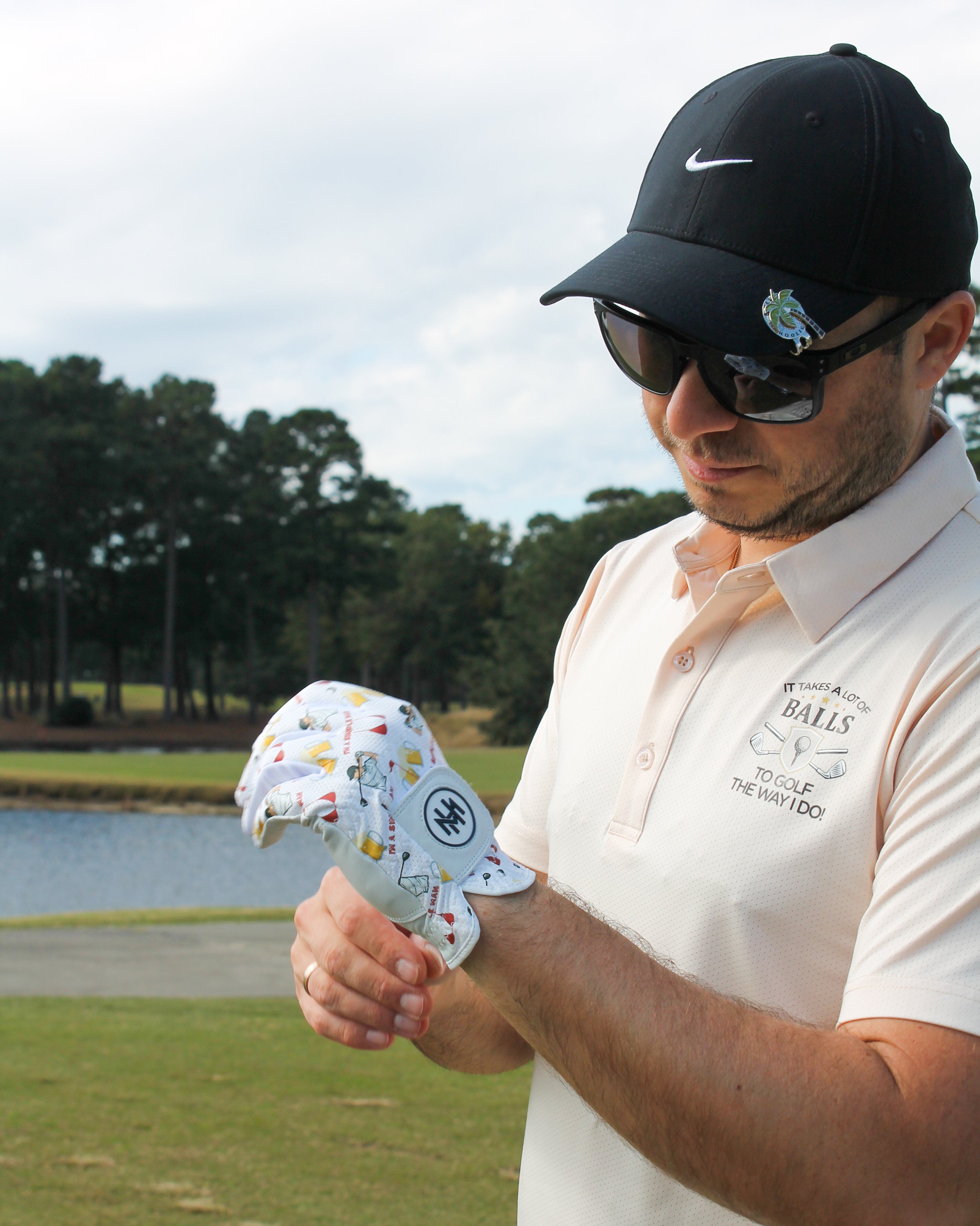 Man on a golf course wearing sunglasses and a Mulligan Hooligan ball marker, admiring the ''I'm a simple man'' golf glove