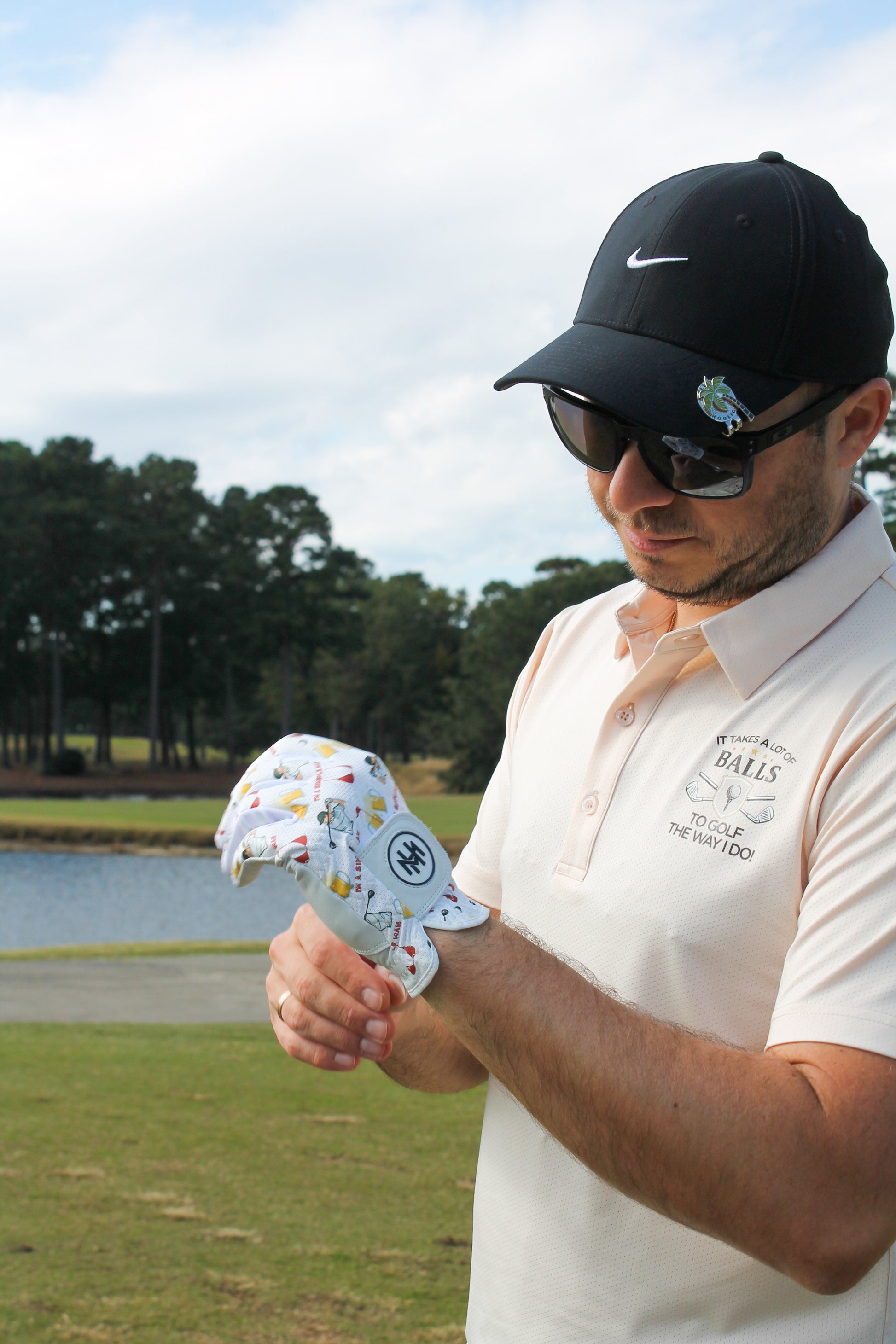 Man on a golf course wearing sunglasses and a Mulligan Hooligan ball marker, admiring the ''I'm a simple man'' golf glove