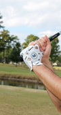 Golf club being held with a Mulligan Hooligan 'Whiskey & Cigars' golf glove on a golf course