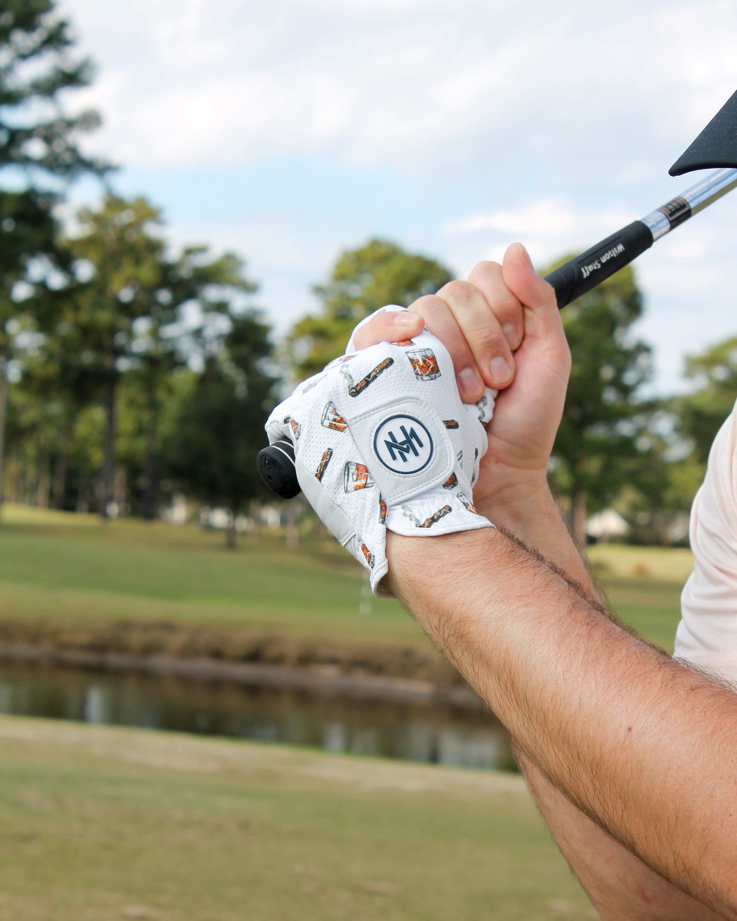 Golf club being held with a Mulligan Hooligan 'Whiskey & Cigars' golf glove on a golf course