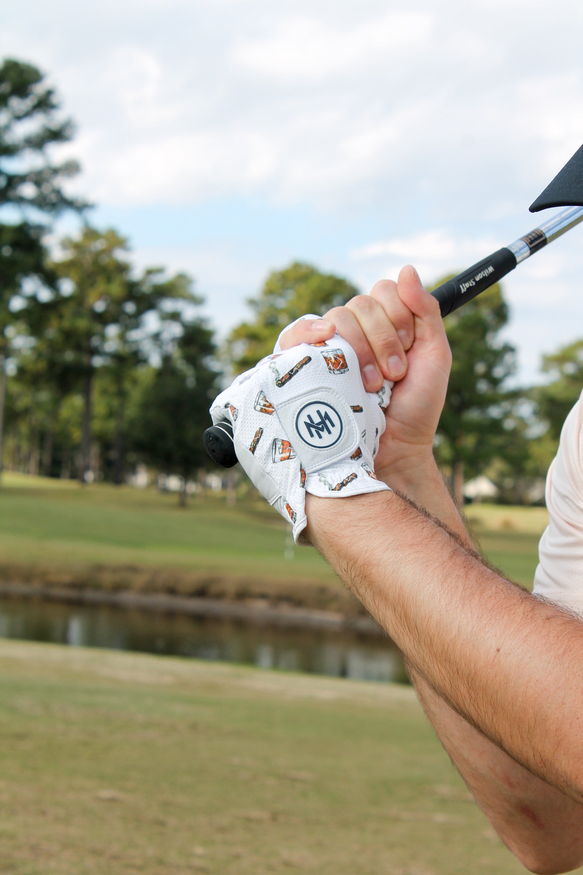 Golf club being held with a Mulligan Hooligan 'Whiskey & Cigars' golf glove on a golf course