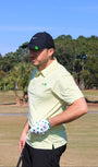 Man on a golf course wearing a green golf polo and the 'Clover Luck' golf glove and the clover ball marker from 'Mulligan Hooligan'