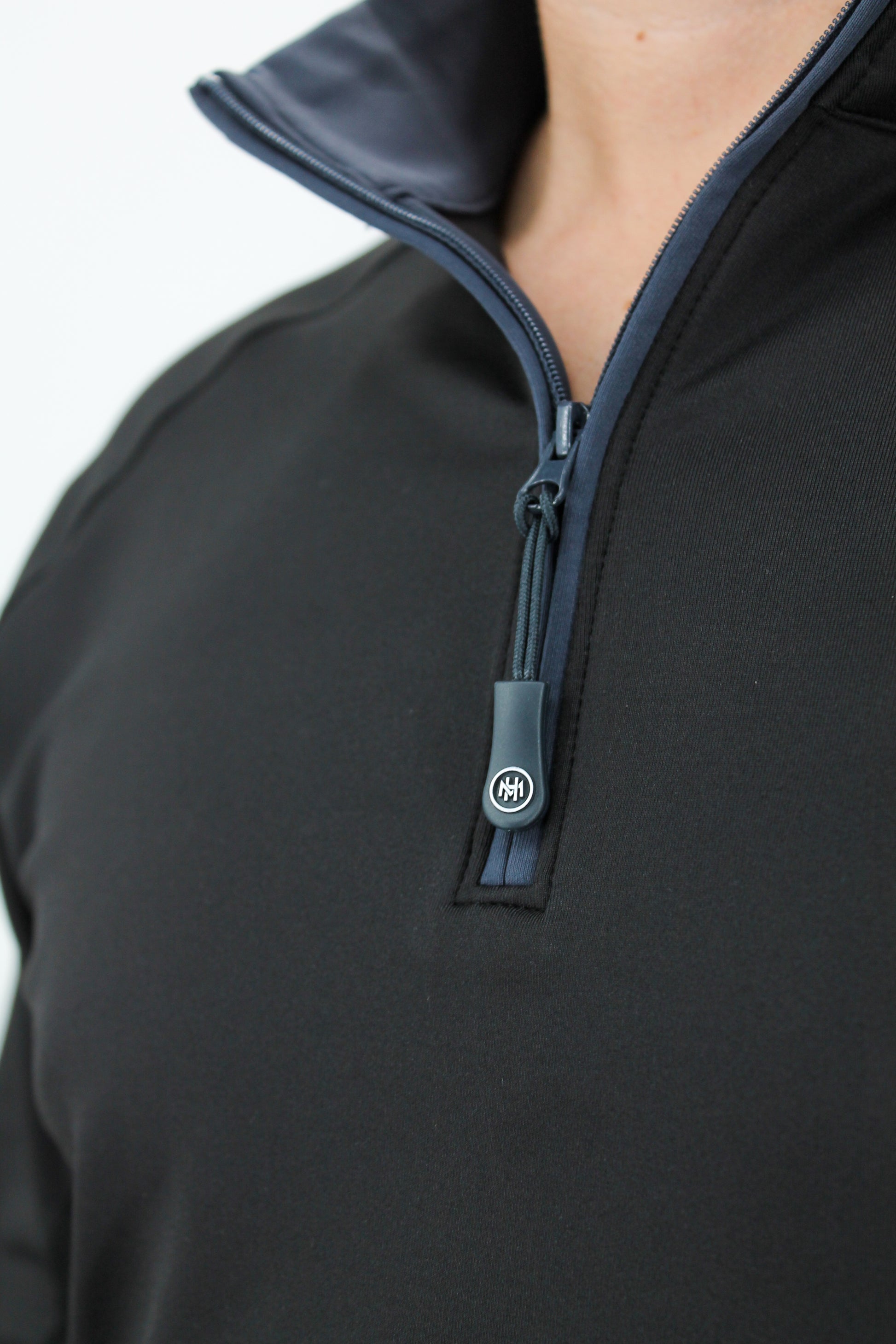 Close-up of a black pullover with a zipper and visible brand logo on a white background
