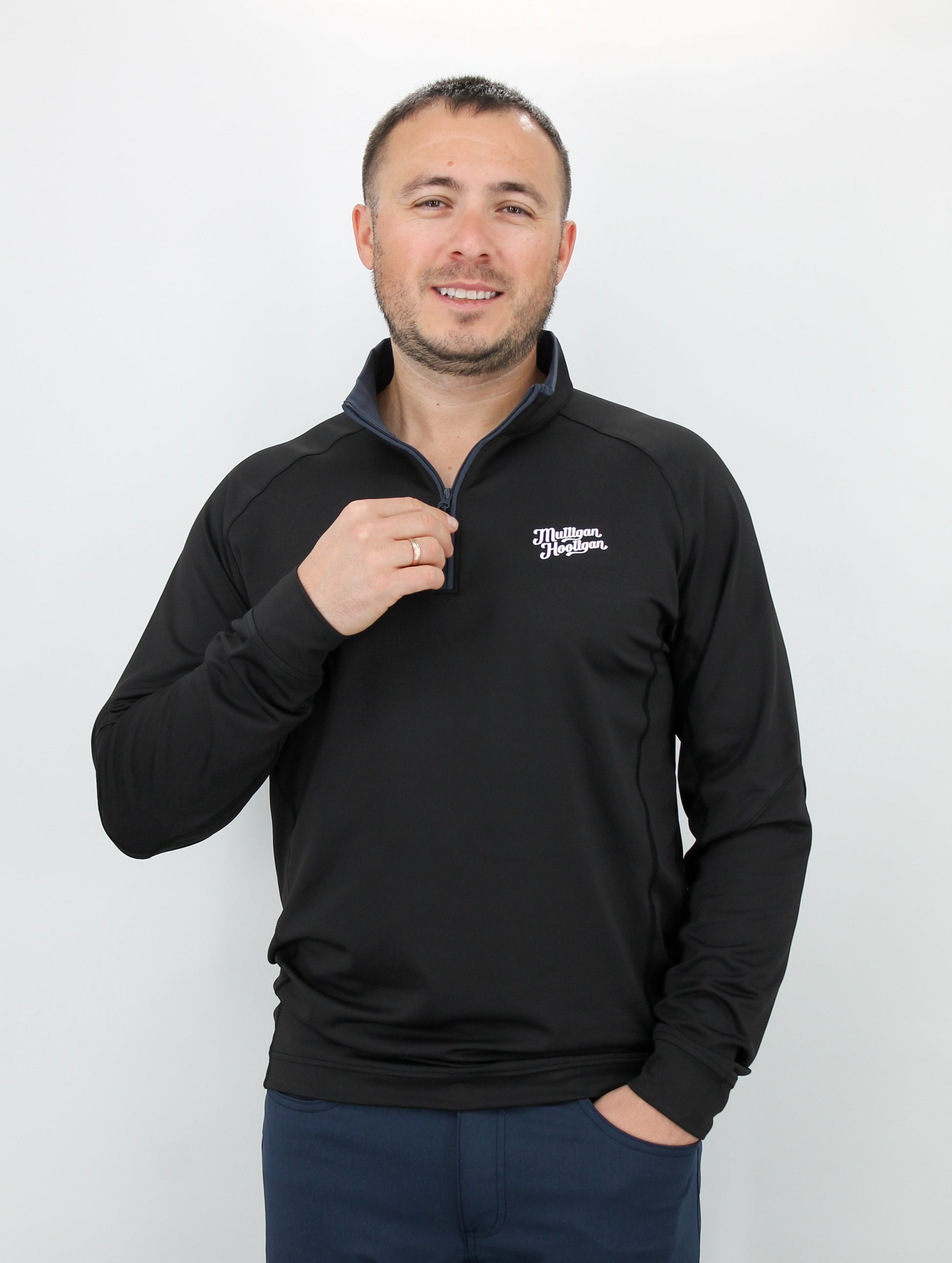 Man wearing a black pullover with 'Mulligan Hooligan' logo on left chest on a white background
