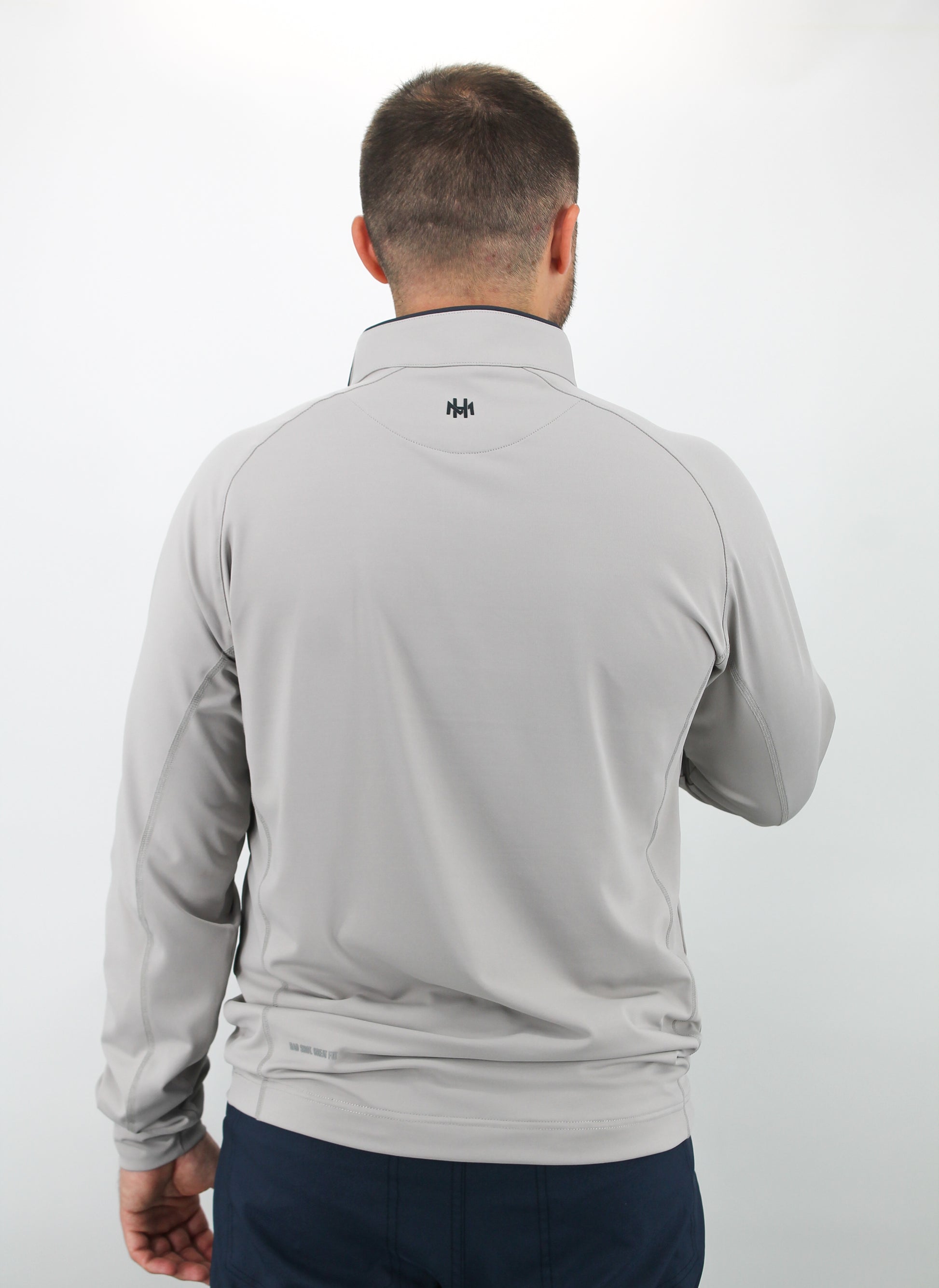 Man wearing a gray long-sleeve shirt with a brand logo on the back against a white background