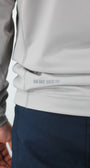 Close-up of a person wearing a light gray jacket and dark blue pants with a visible brand logo.