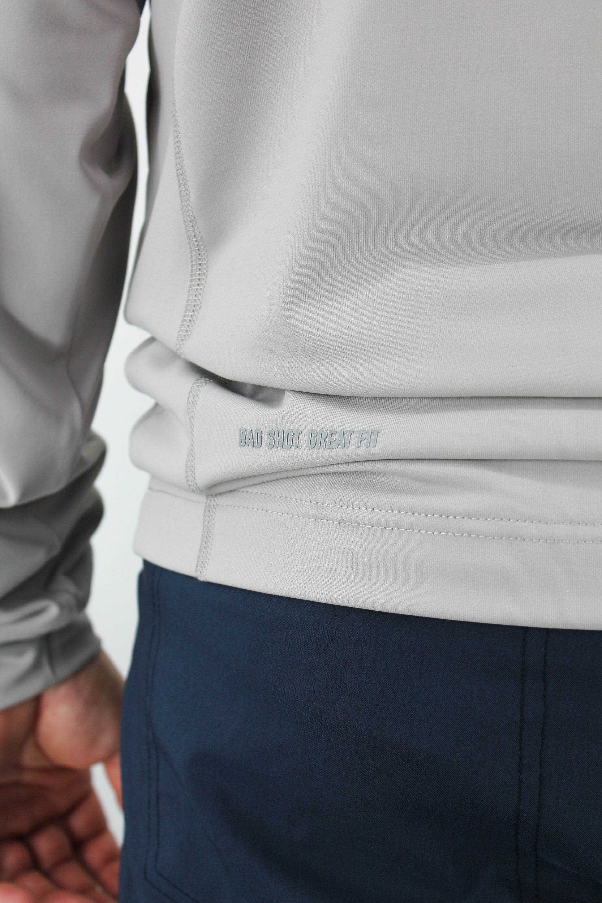 Close-up of a person wearing a light gray jacket and dark blue pants with a visible brand logo.