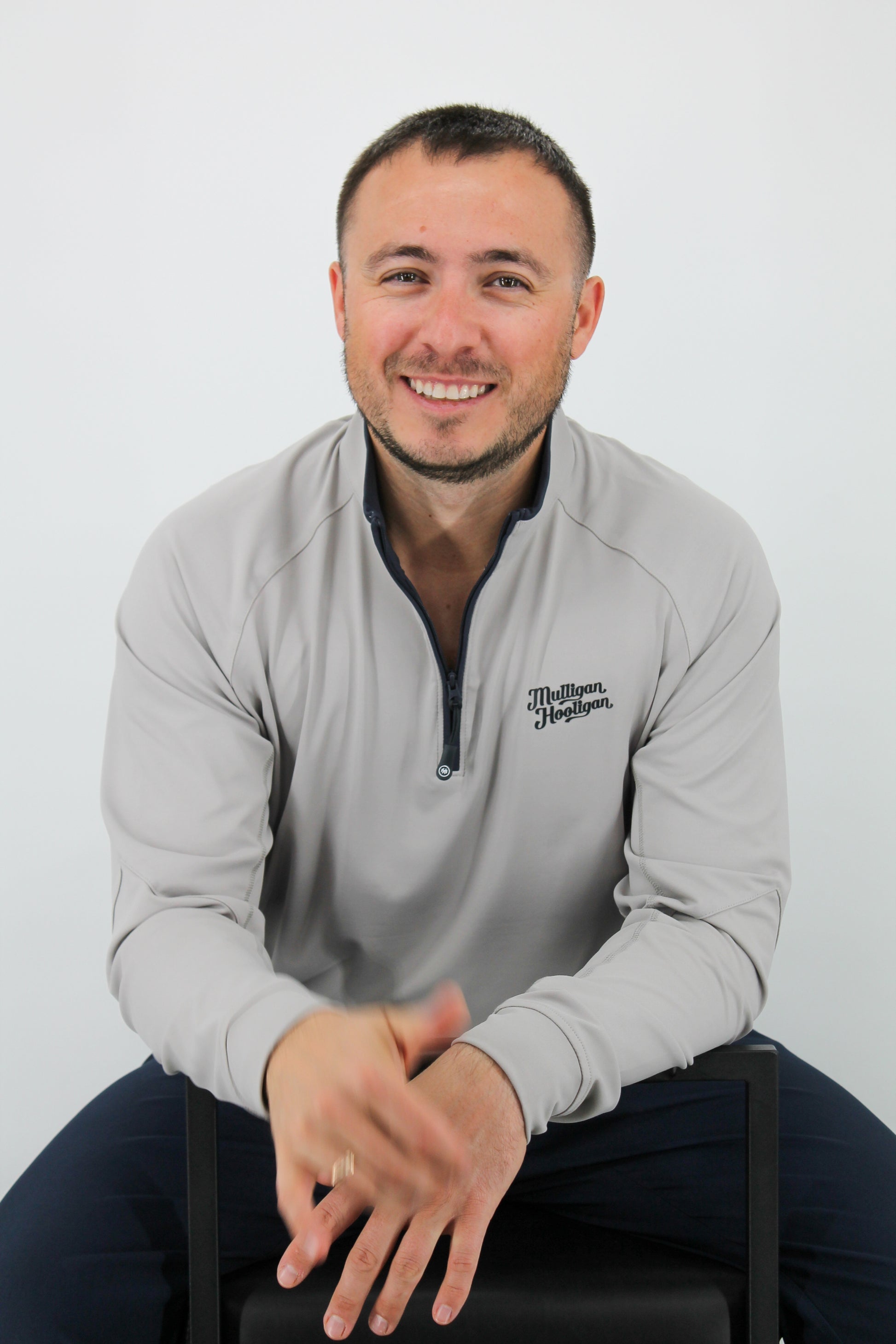 Man wearing a gray sweatshirt with a logo, sitting on a white background