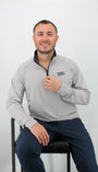 Man wearing a gray pullover with a logo, sitting on a chair against a white background