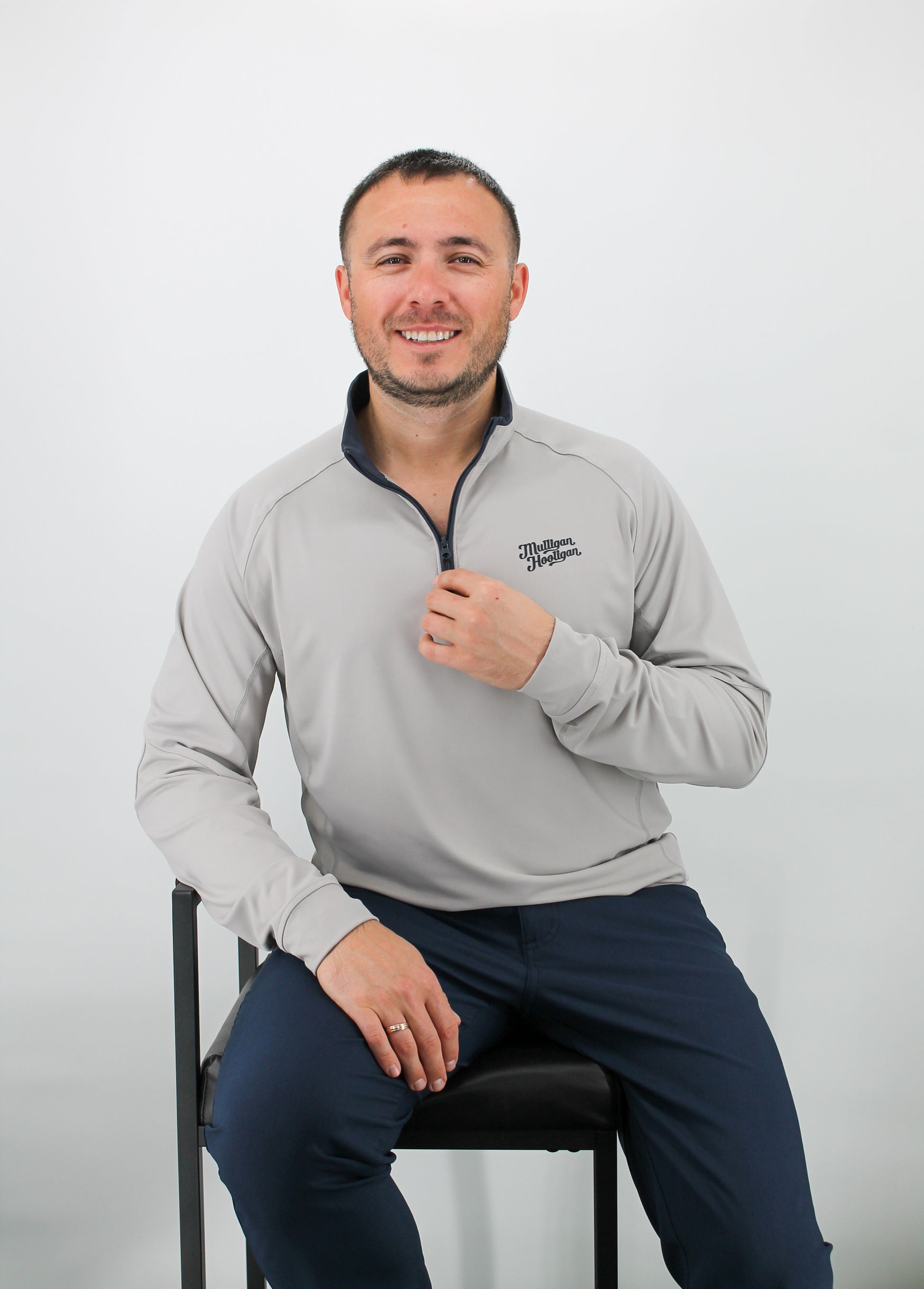 Man wearing a gray pullover with a logo, sitting on a chair against a white background