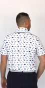 A man viewed from behind wearing a white short-sleeve collared shirt with a patriotic-theme all-over print of small blue, red, and gray icons, paired with dark navy pants, against a plain white background.