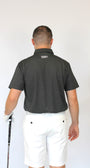 A man viewed from behind wearing a dark charcoal gray short-sleeve polo shirt and white shorts, holding a golf club against a plain white background.