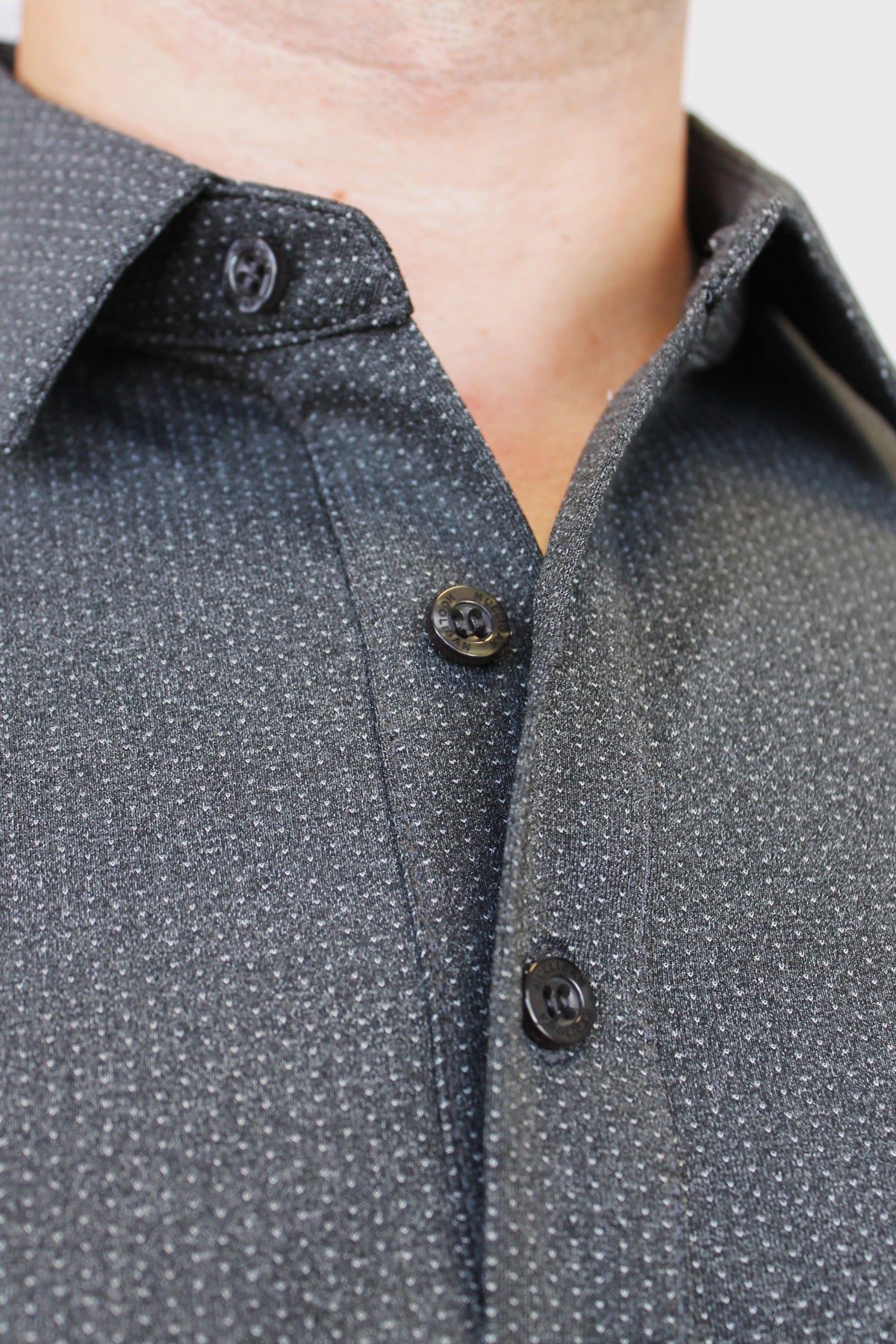 Close-up of a dark gray micro-patterned button-down shirt worn by a model, showing the collar, buttons, and textured fabric.
