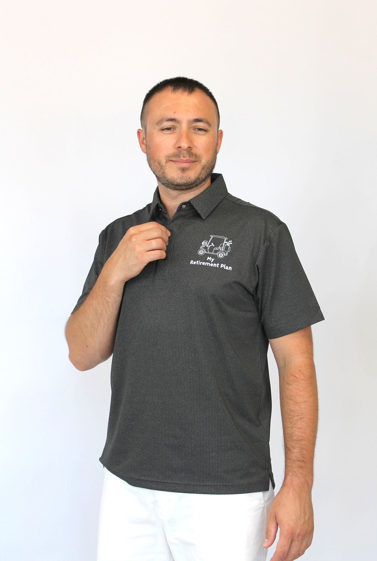 A man wearing a dark gray short-sleeve polo shirt with a white embroidered logo on the left chest, paired with white pants, standing against a plain white background.