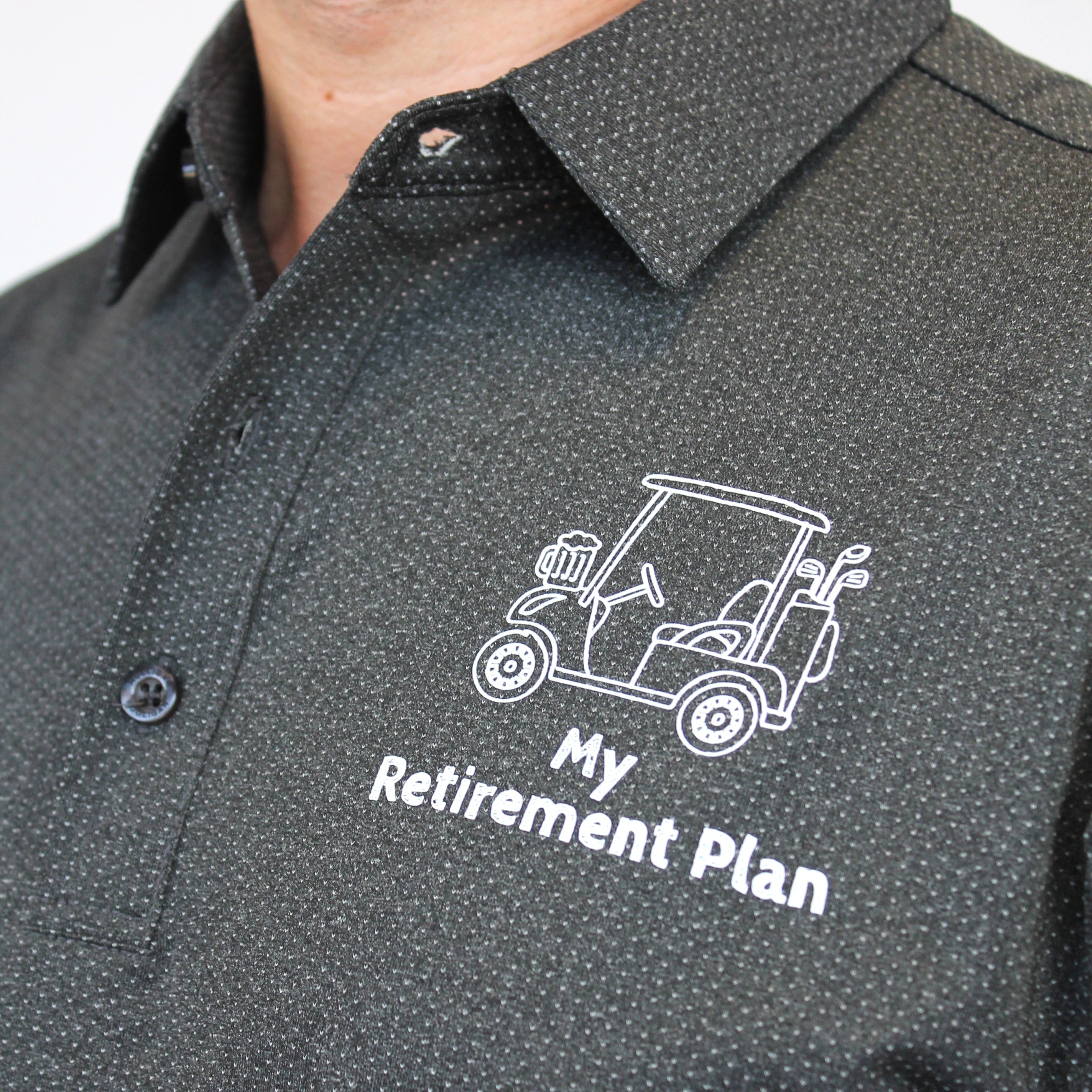 A close-up of a man wearing a dark gray micro-patterned button-down shirt with a white printed golf cart and the text 'My Retirement Plan' on the chest.