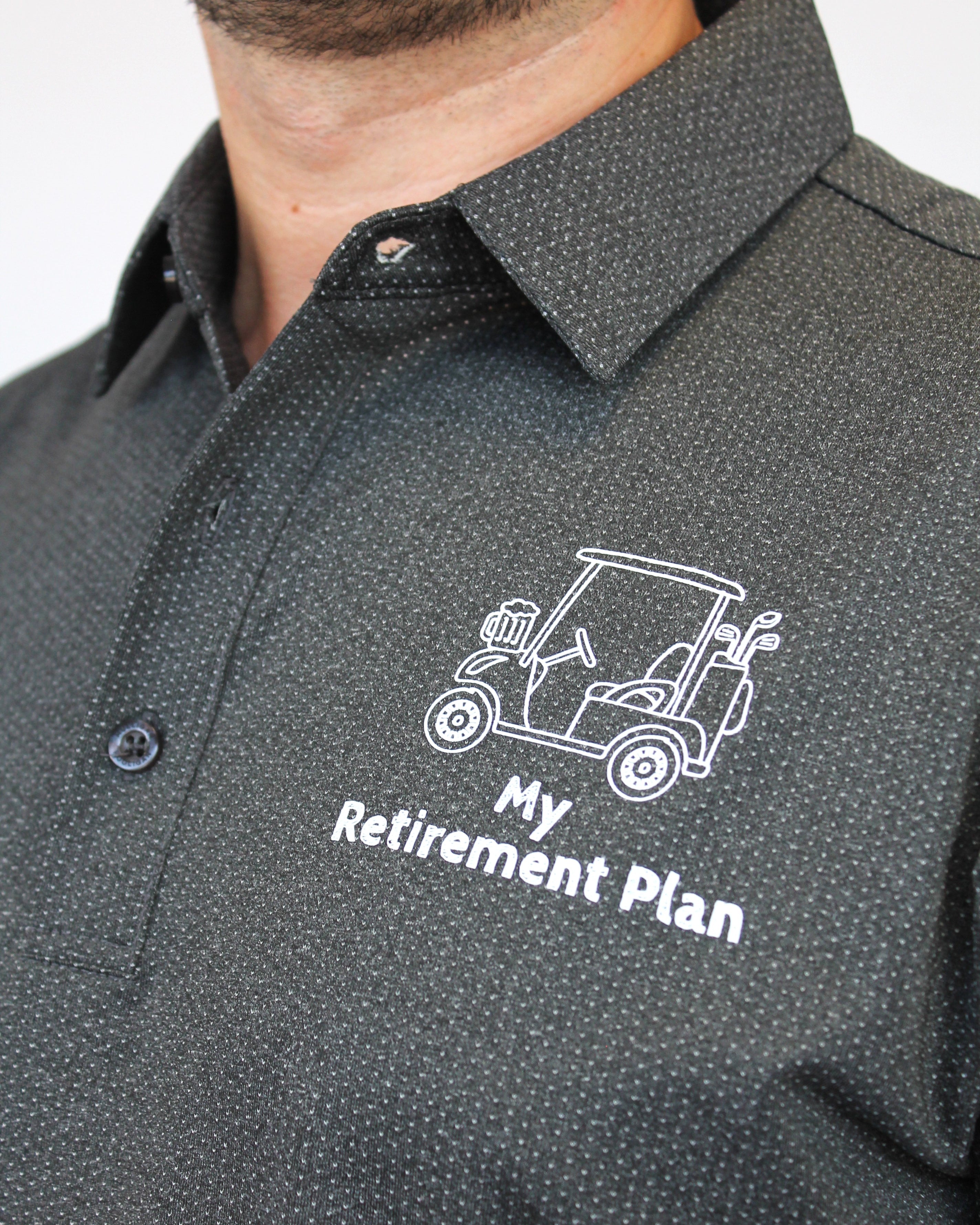A close-up of a man wearing a dark gray micro-patterned button-down shirt with a white printed golf cart and the text 'My Retirement Plan' on the chest.