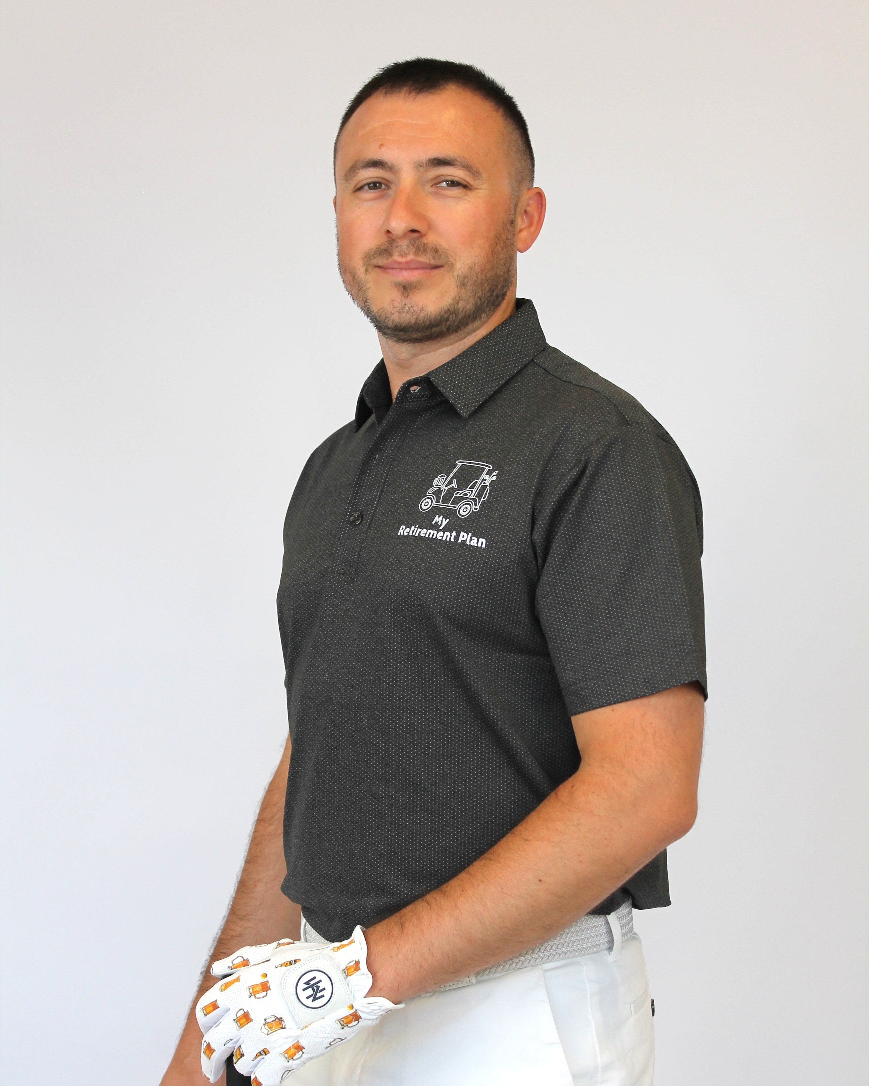 A man wearing a dark gray short-sleeve polo shirt with a white golf club and white pants, holding the club with a white golf glove. The polo shirt features a white logo on the left chest that reads 'My Retirement Plan'.