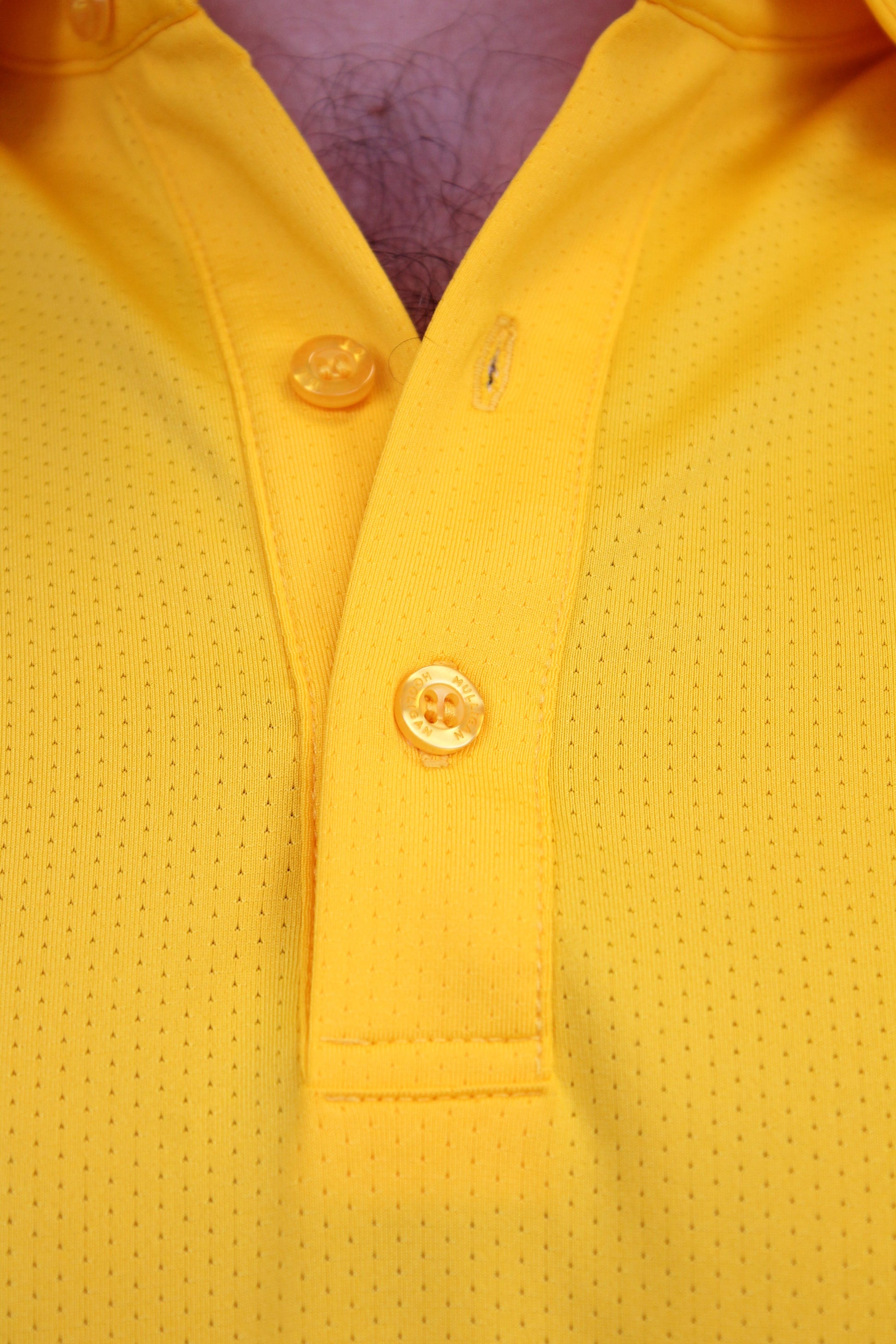 Close-up of a bright yellow perforated polo shirt showing the collar, 3 yellow buttons, and a textured fabric surface.