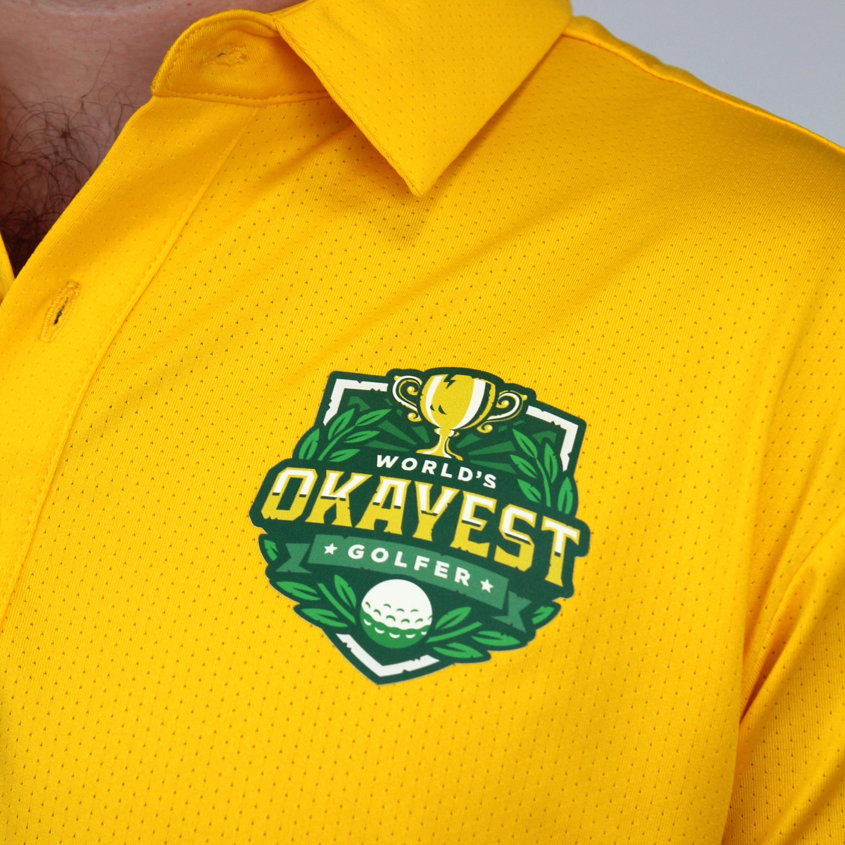 Close-up of a person wearing a bright yellow polo shirt with a green and gold 'World's Okayest Golfer' chest graphic.