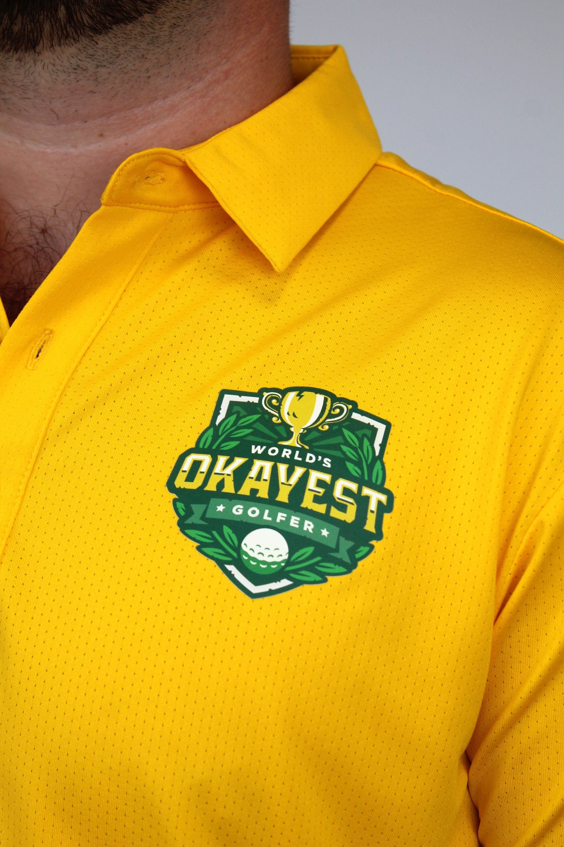 Close-up of a person wearing a bright yellow polo shirt with a green and gold 'World's Okayest Golfer' chest graphic.
