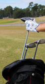 A hand in a Mulligan Hooligan "Palm Par" golf glove pulling a golf club out of a bag on a golf course.