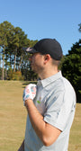 Man on a golf course with a golf glove and a Mulligan Hooligan Polo with a clear blue sky and trees in the background