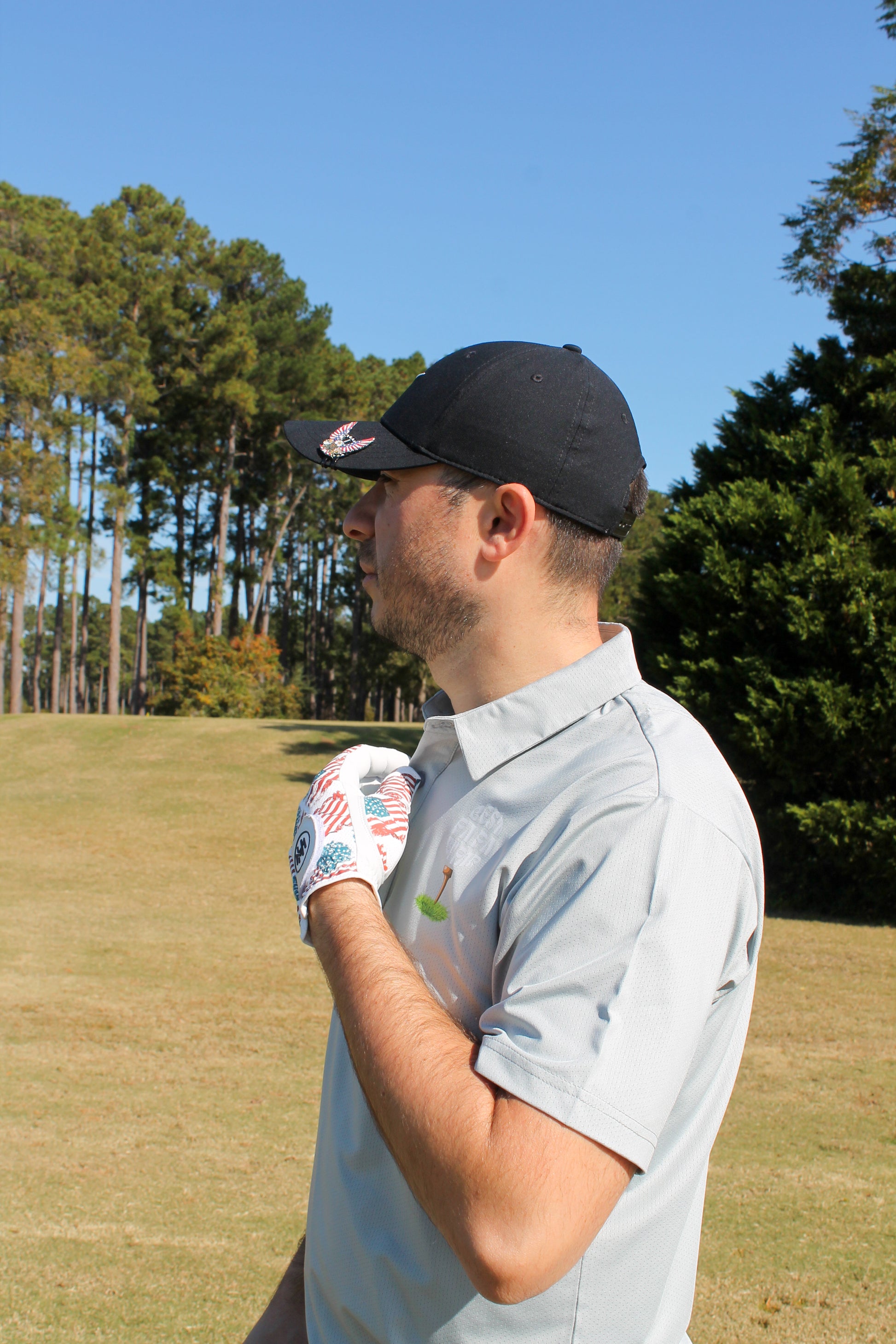Man on a golf course with a golf glove and a Mulligan Hooligan Polo with a clear blue sky and trees in the background