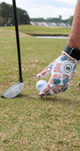 A person hand on a golf course with the Patriotic USA Flag glove setting the golf ball on the tee and golf club