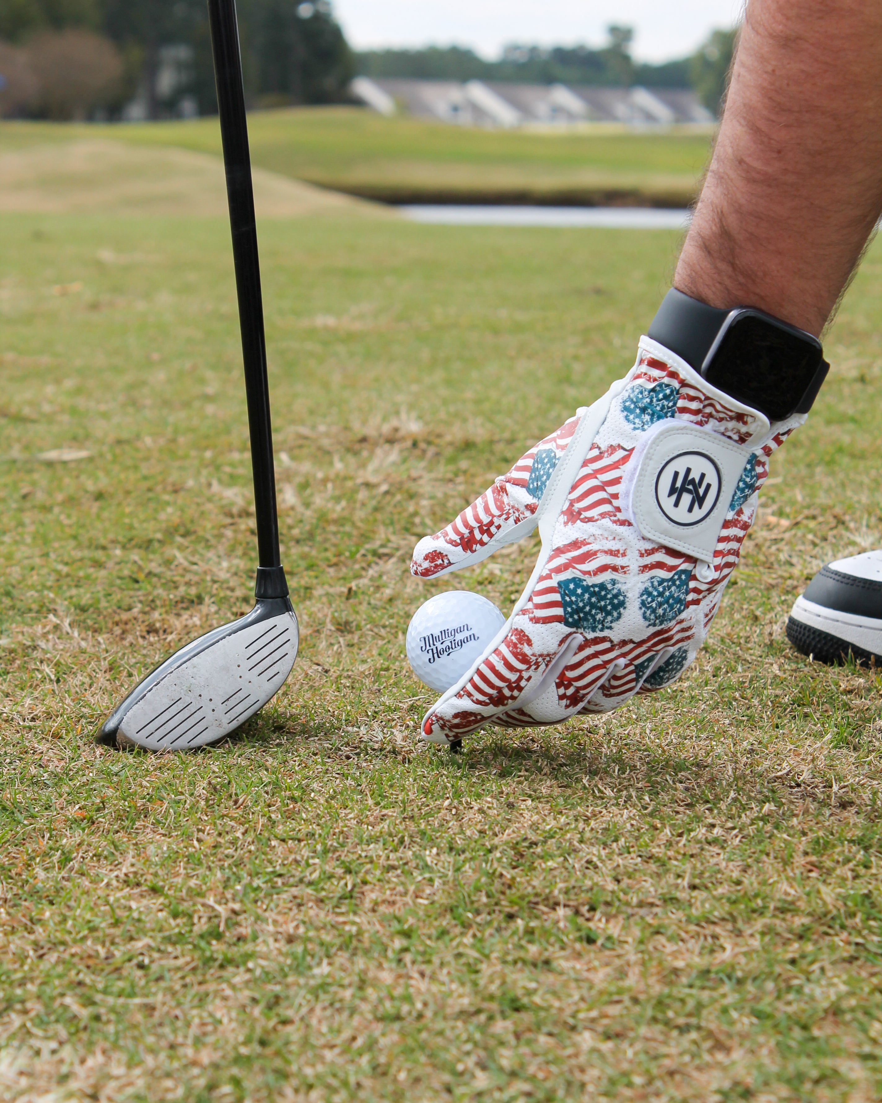 A person hand on a golf course with the Patriotic USA Flag glove setting the golf ball on the tee and golf club