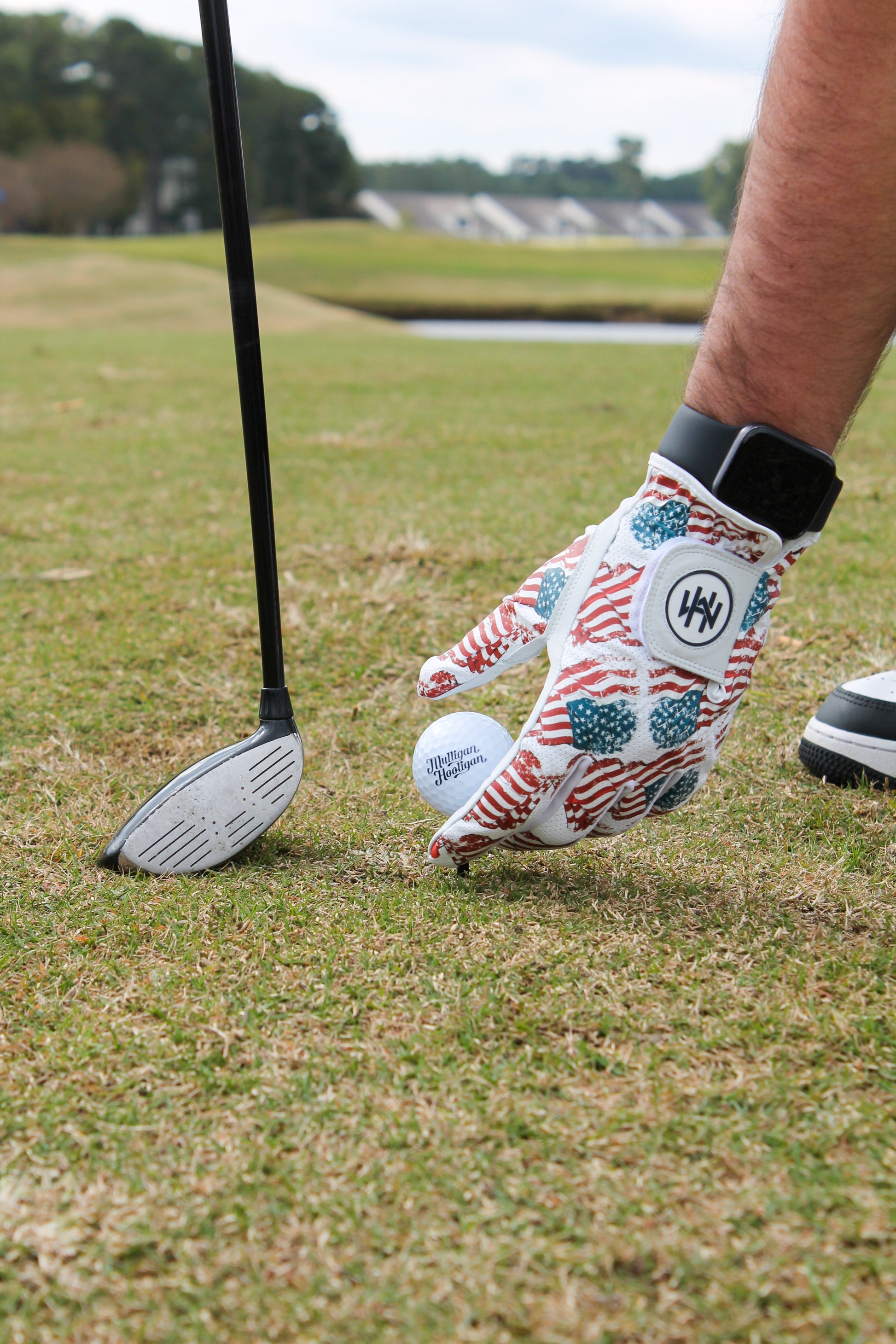 A person hand on a golf course with the Patriotic USA Flag glove setting the golf ball on the tee and golf club