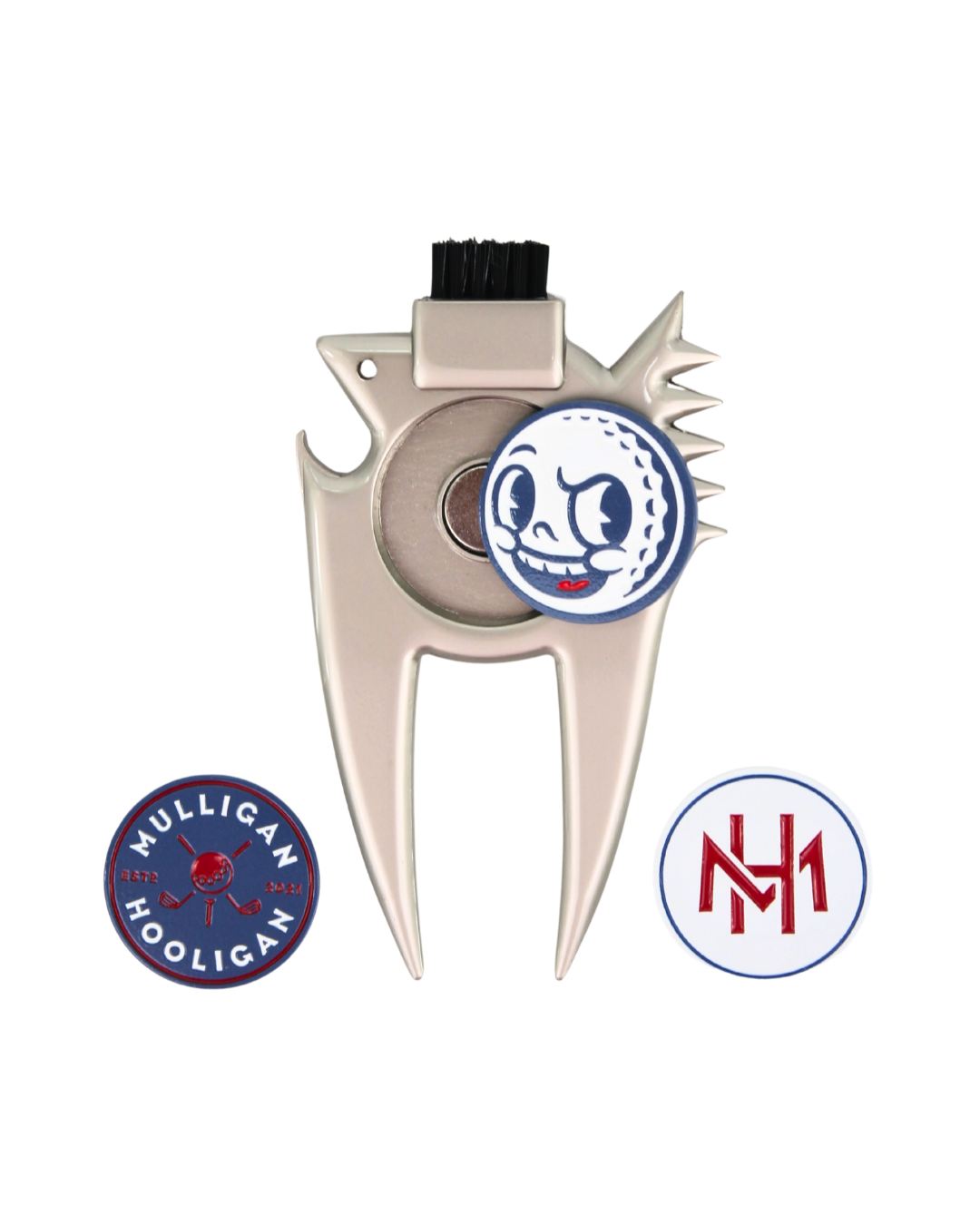 A silver metal golf divot tool with a black bristle brush on top, featuring a circular golf ball graphic with a cartoon face on the center. Two circular decals are shown below: one blue and red reading 'MULLIGAN HOOLIGAN' and one white and red with 'MH'.