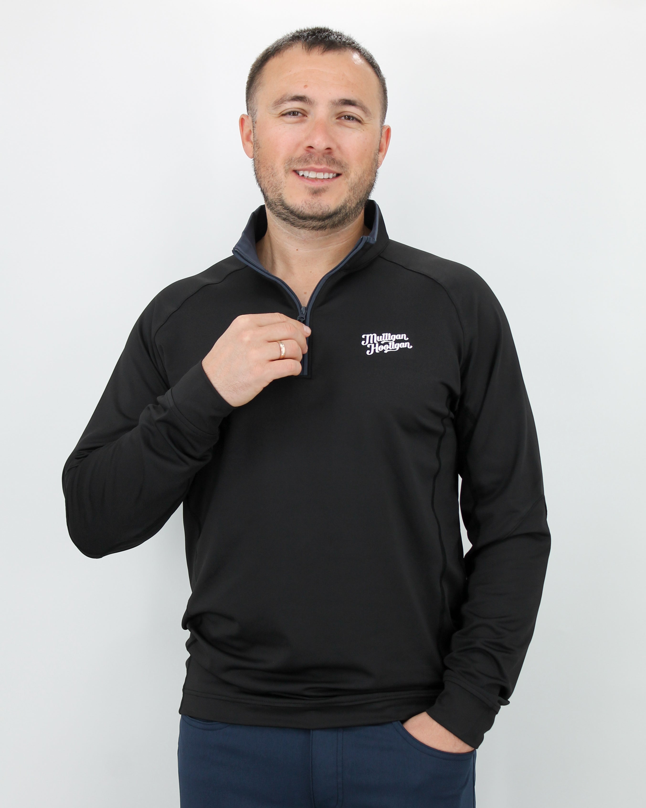 Man wearing a black pullover with 'Mulligan Hooligan' logo on left chest on a white background