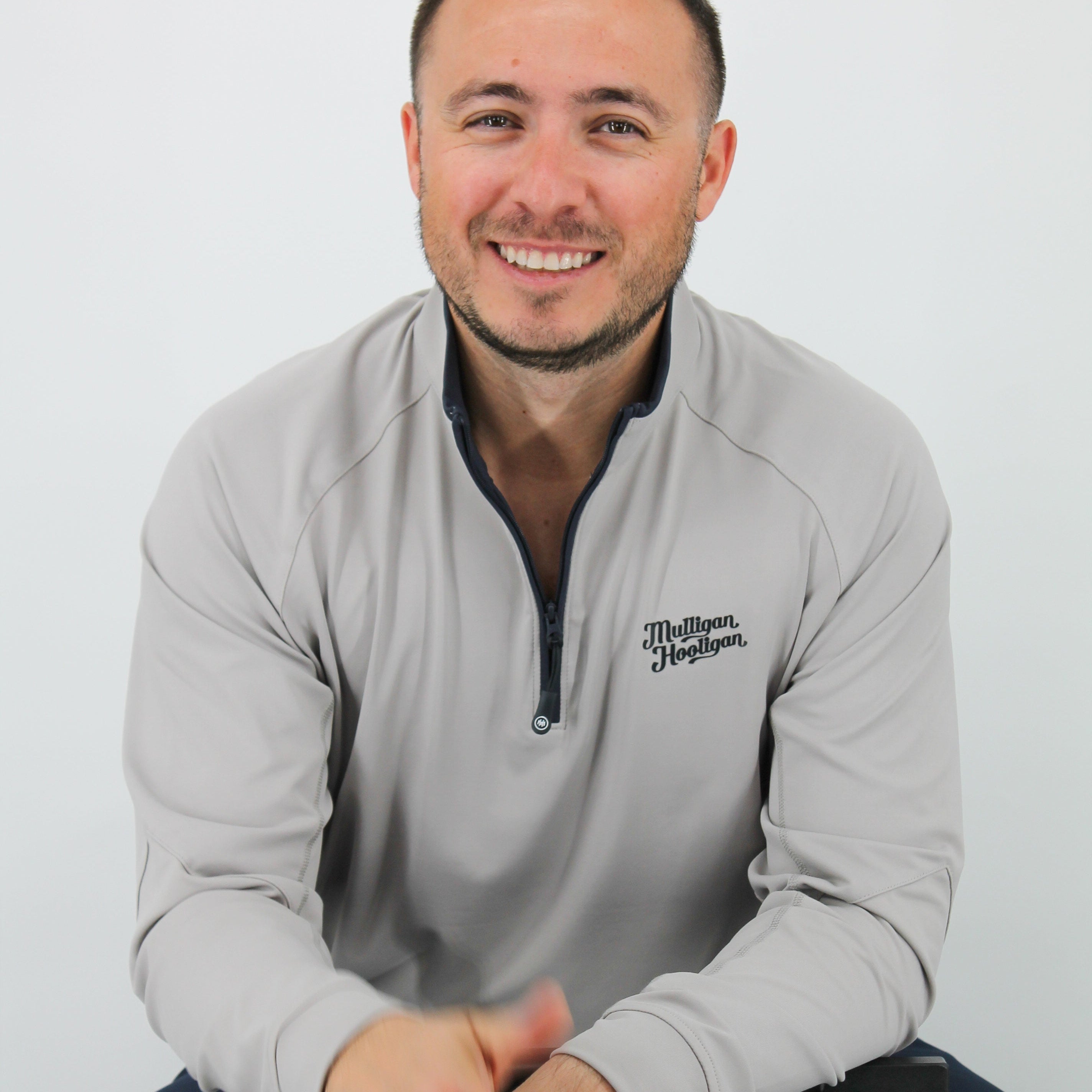 Man wearing a gray sweatshirt with a logo, sitting on a white background