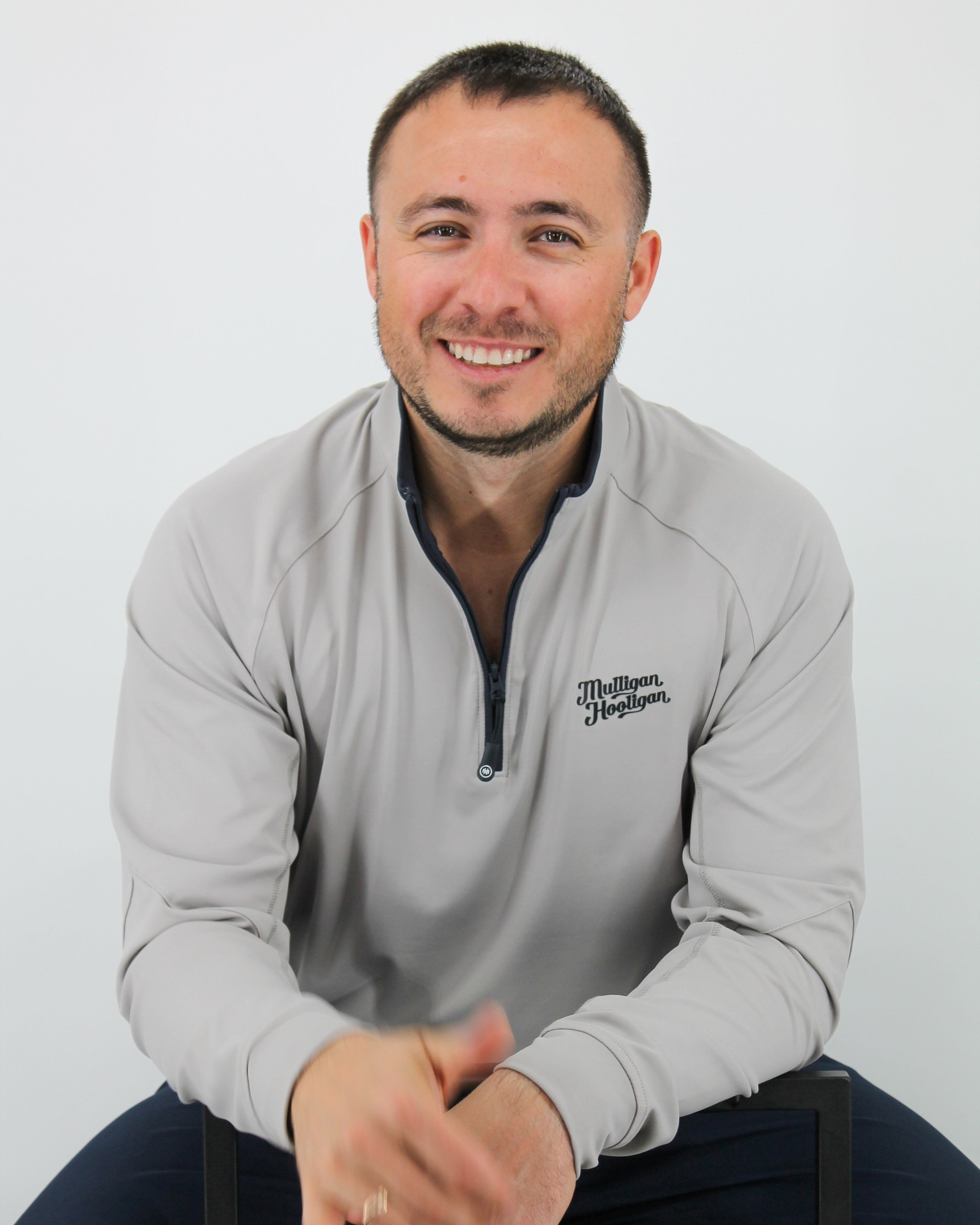 Man wearing a gray sweatshirt with a logo, sitting on a white background