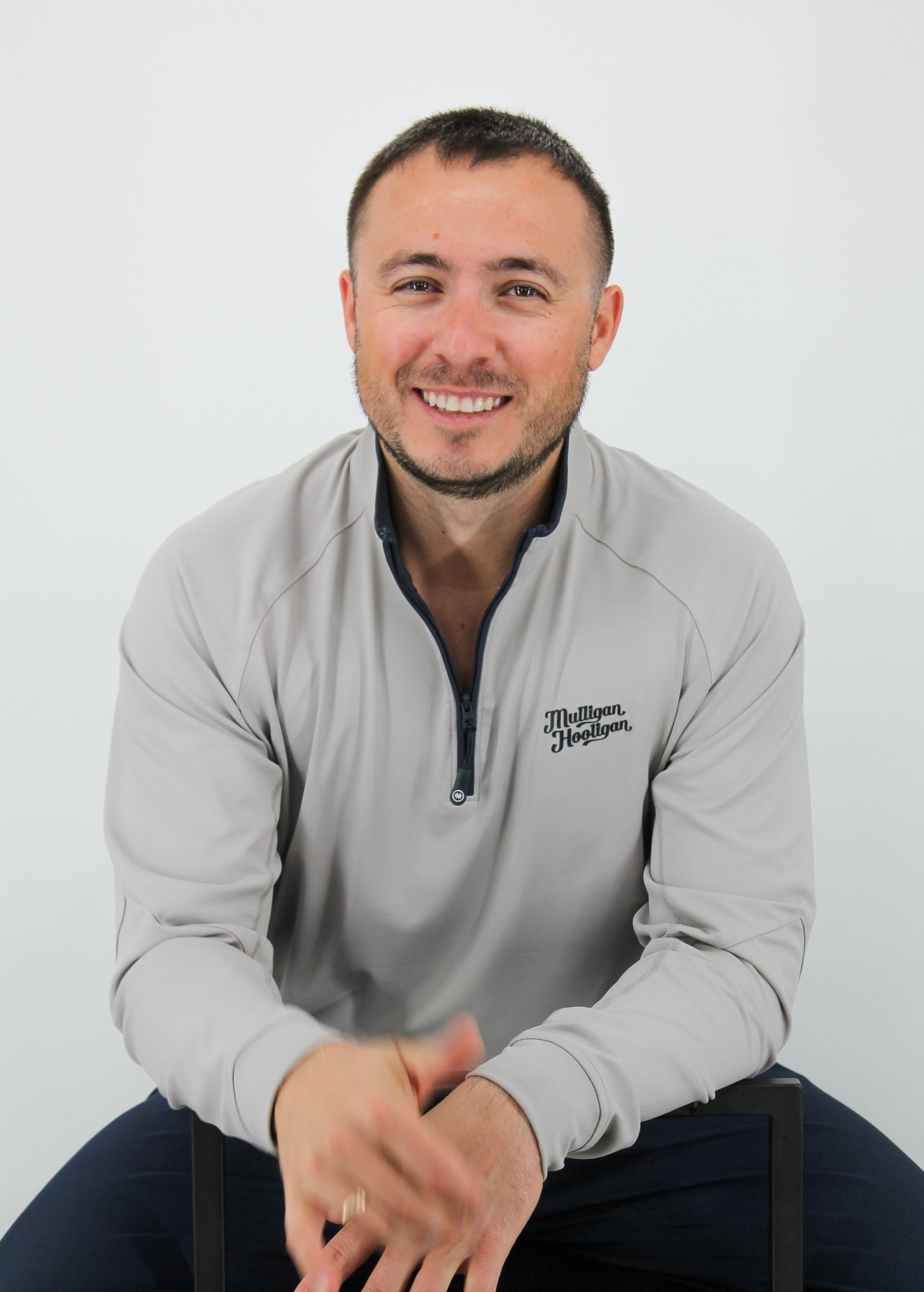 Man wearing a gray sweatshirt with a logo, sitting on a white background